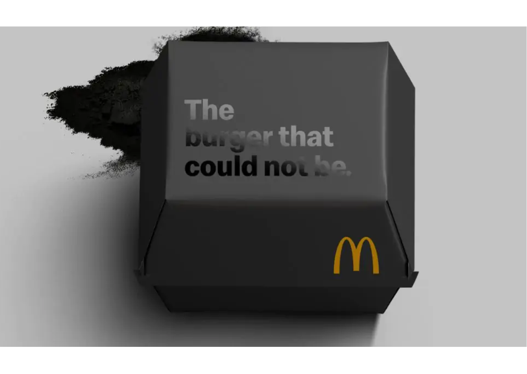 Črna embalaža za burger z logotipom McDonald’s in napisom ‘The burger that could not be.’, iz katere se na levi strani razpršuje temen prah.