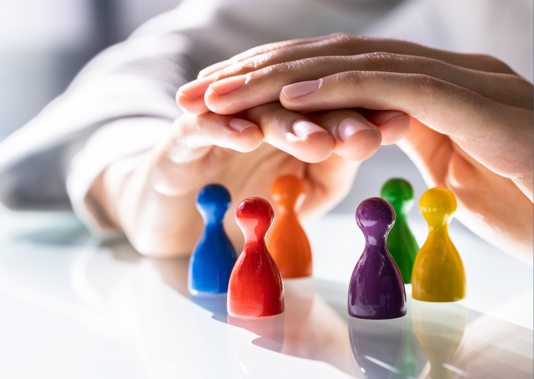 Roke zaščitniško pokrivajo več barvnih figuric ljudi, razporejenih na površini.